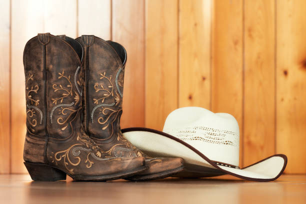 cowgirl embroidered boots and white hat on wooden background – text space